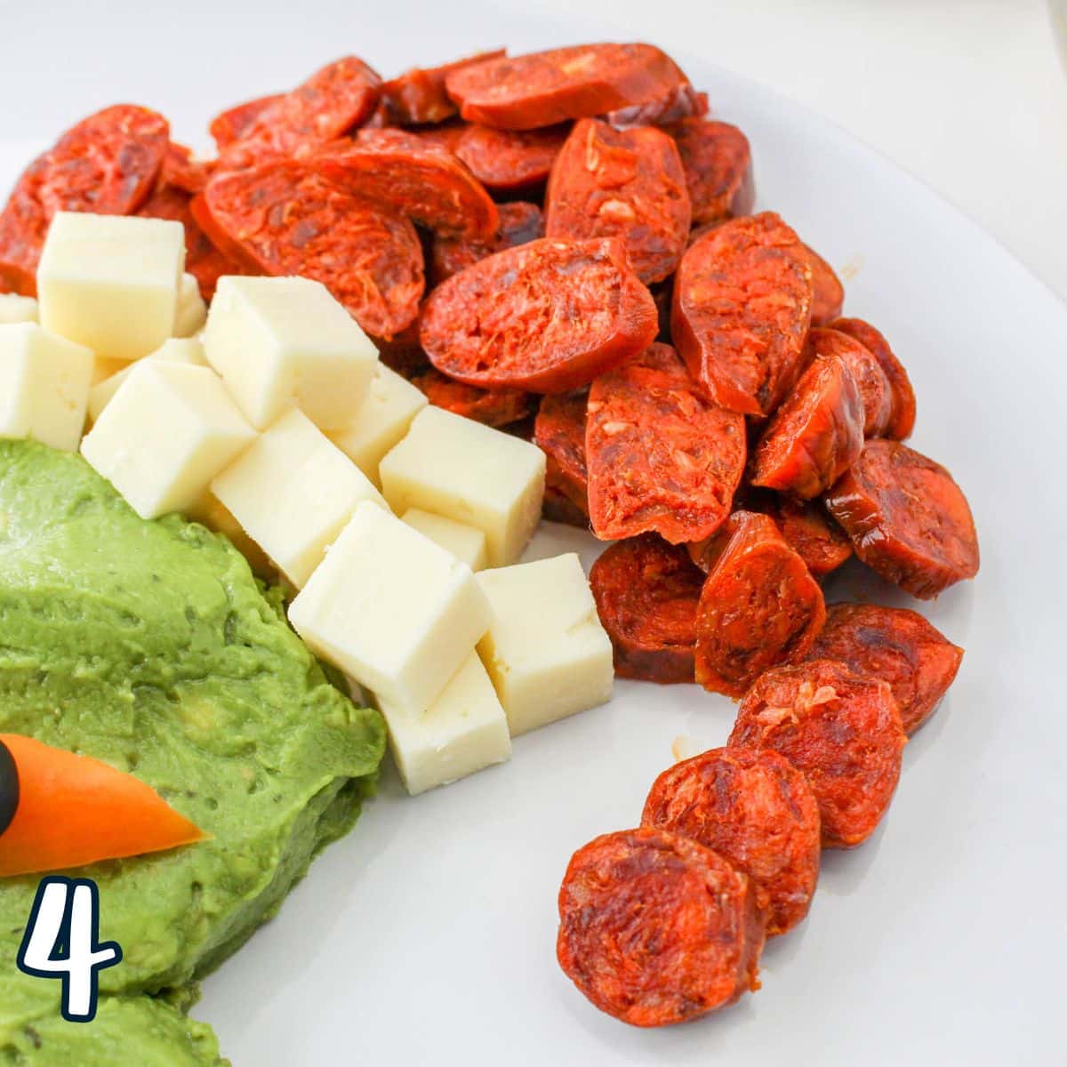 Guacamole on a white plate with cheese and chorizo.