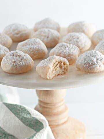 Powdered sugar cookies on a white plate with a bite taken out of it.