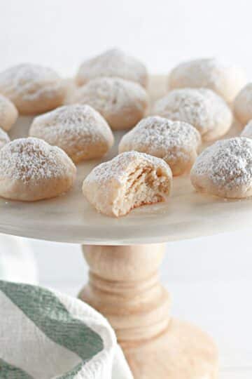 Powdered sugar cookies on a white plate with a bite taken out of it.