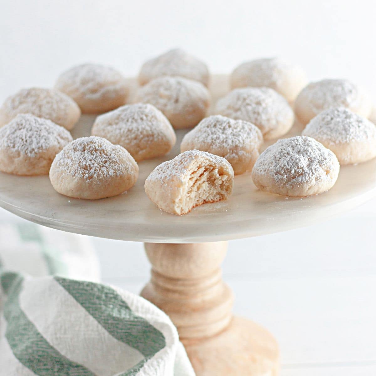 Powdered sugar cookies on a white plate with a bite taken out of it.