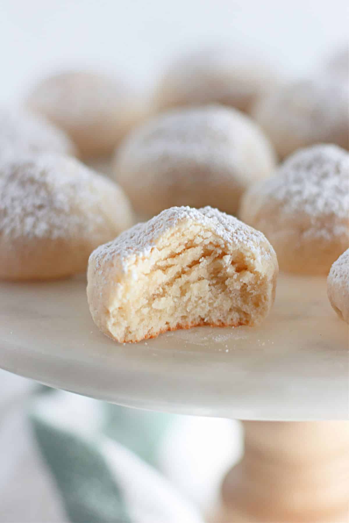 Powdered sugar cookies on a white plate with a bite taken out of them.