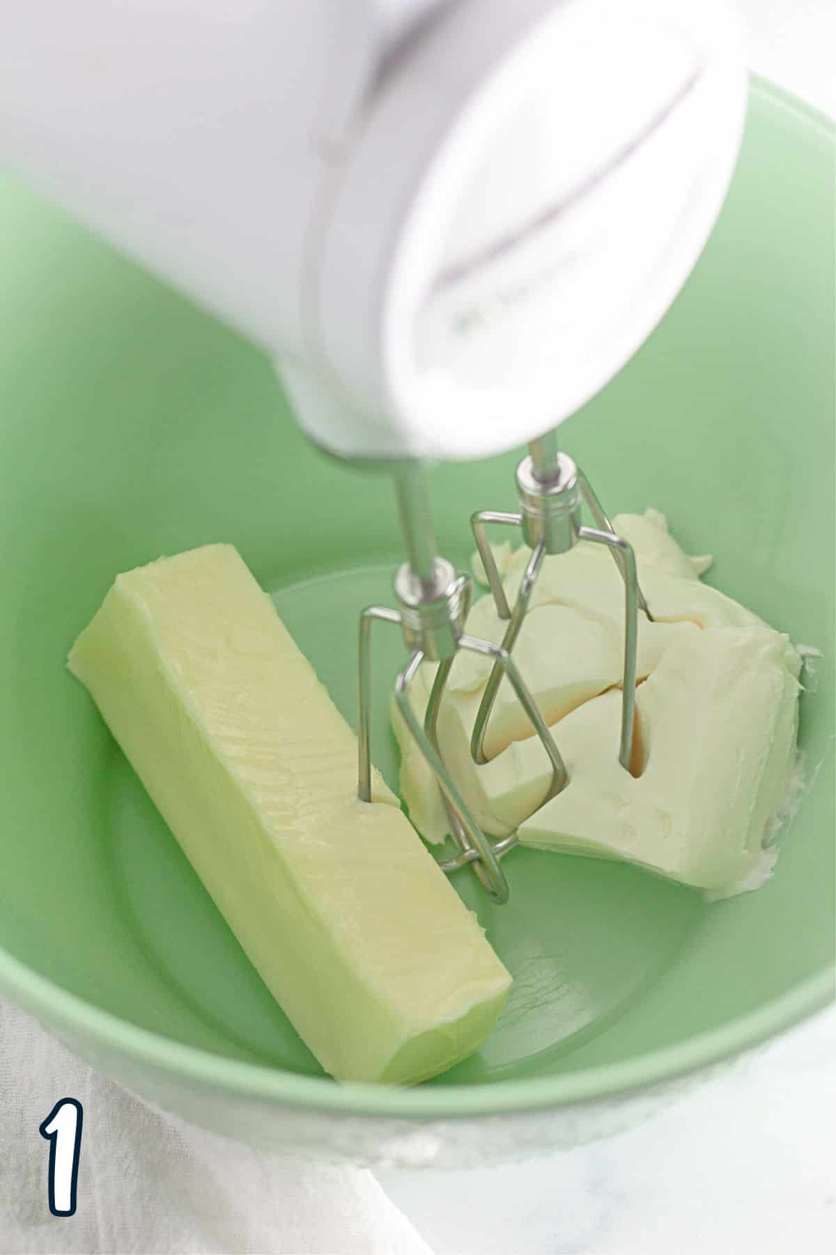 A green bowl with butter  and a mixer in it.