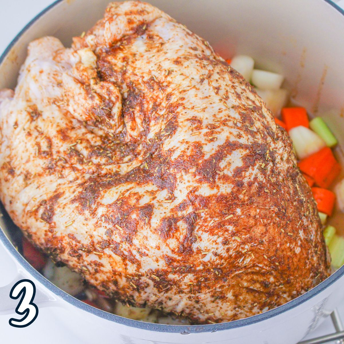 A whole turkey breast rub with spices in a pot with vegetables.