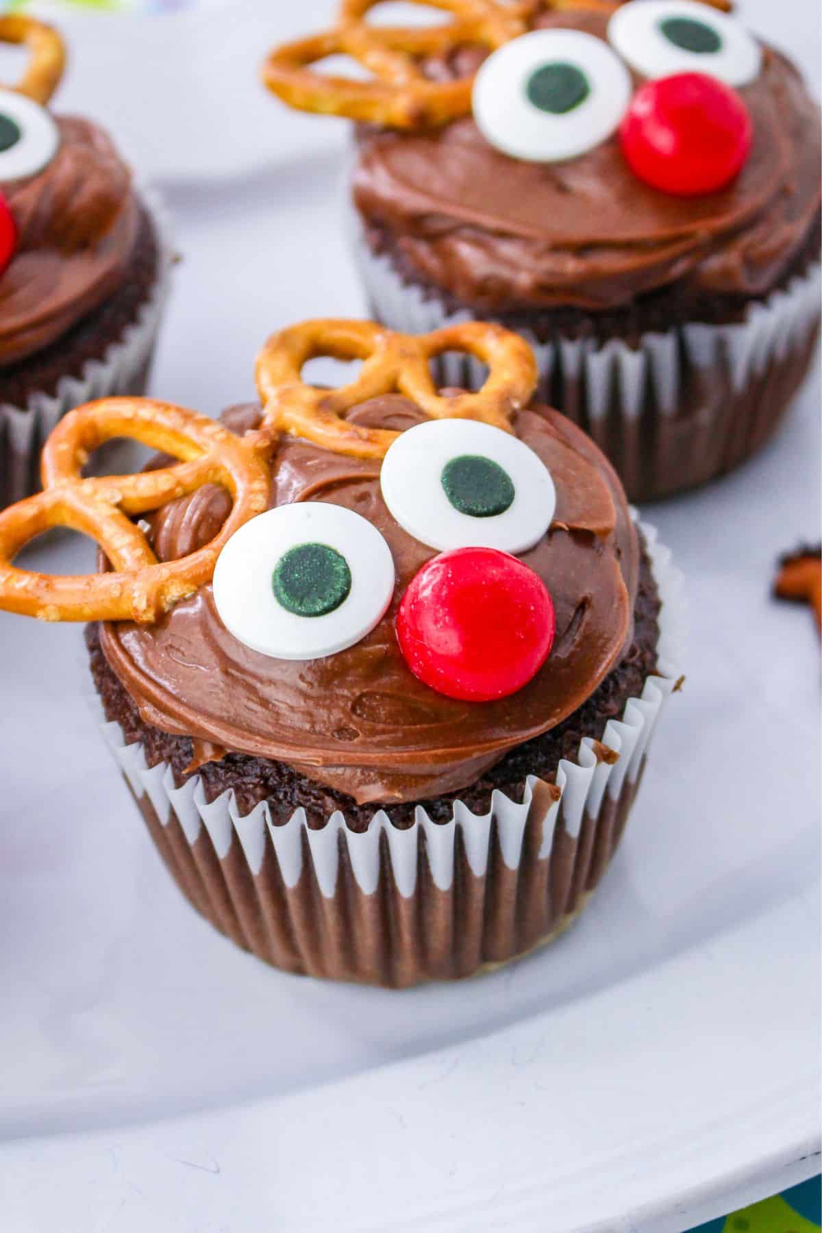 Chocolate reindeer cupcakes with pretzel antlers on a white plate.