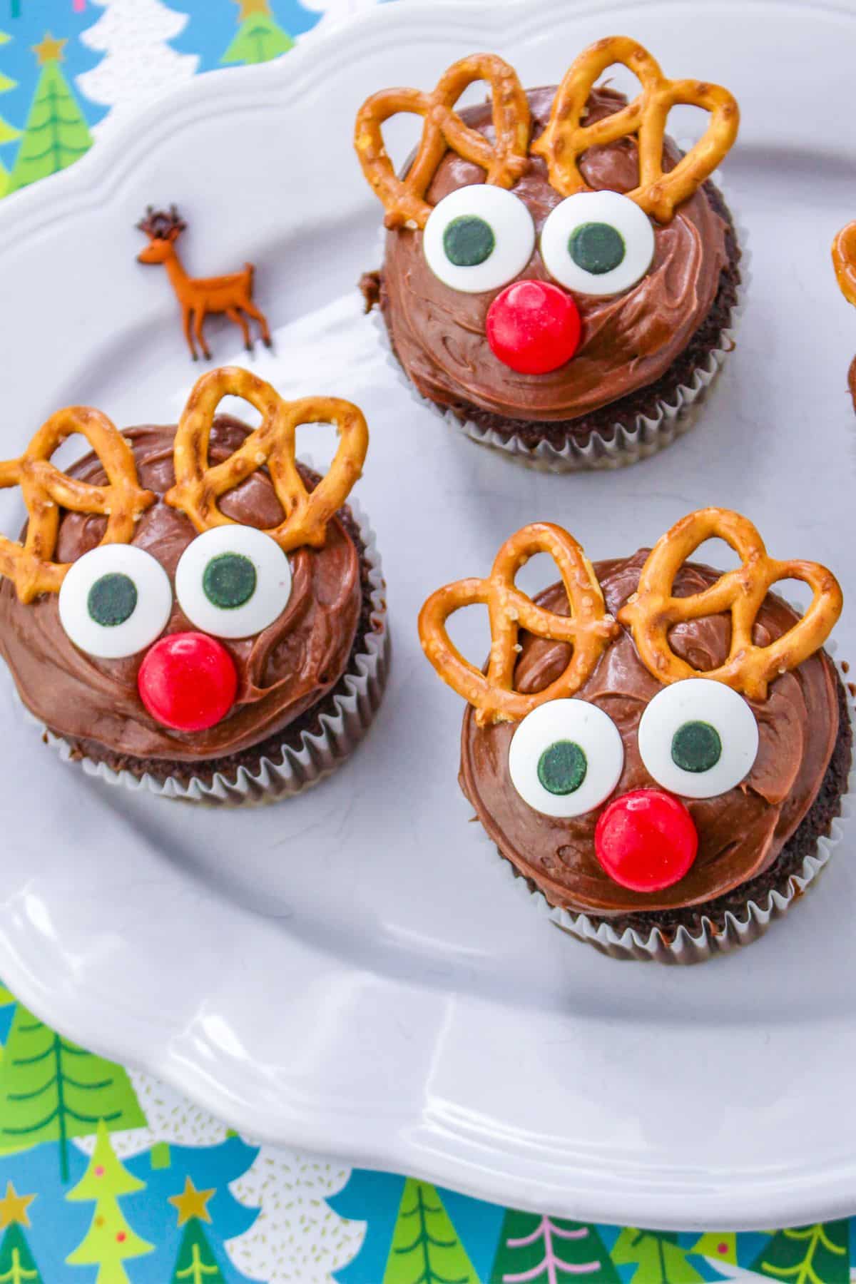 Reindeer cupcakes with pretzel antlers and red noses on a plate.
