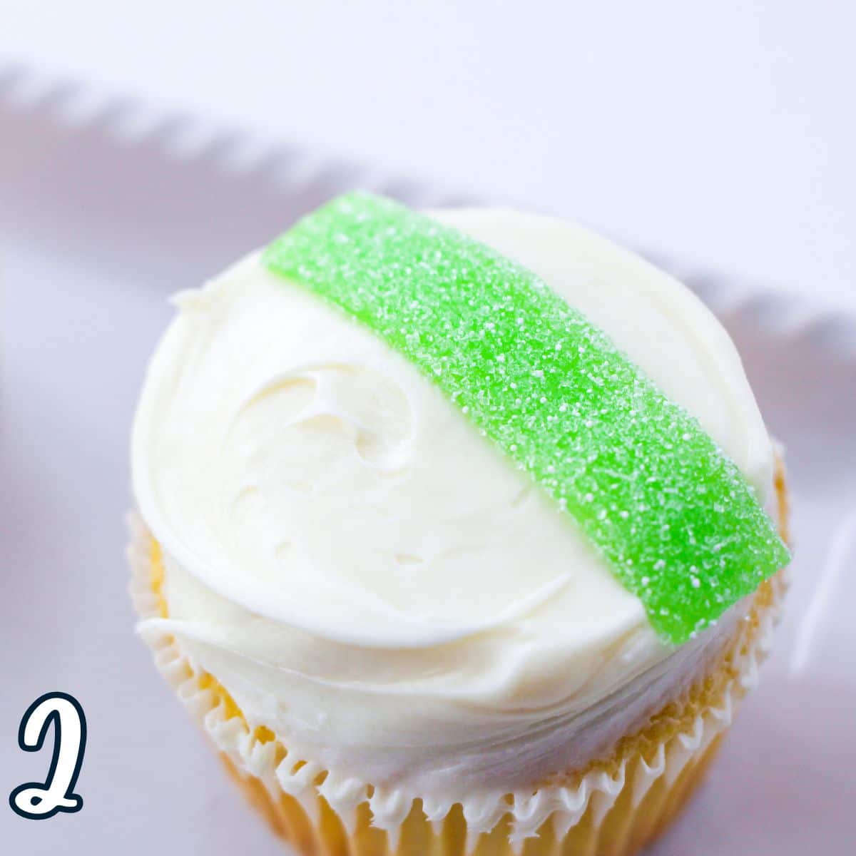 A cupcake with white frosting and a green gummy streamer on a plate.