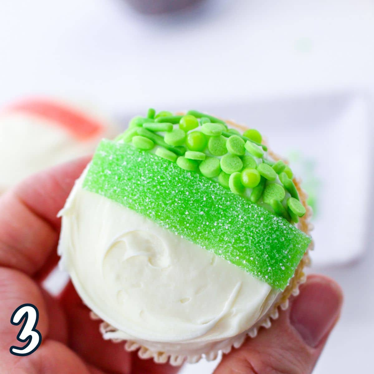 A person holding a cupcake with a green gummy streamer and green sprinkles.