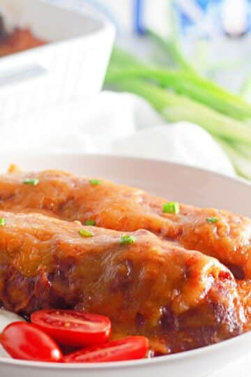 A plate of enchiladas with sour cream and tomatoes.