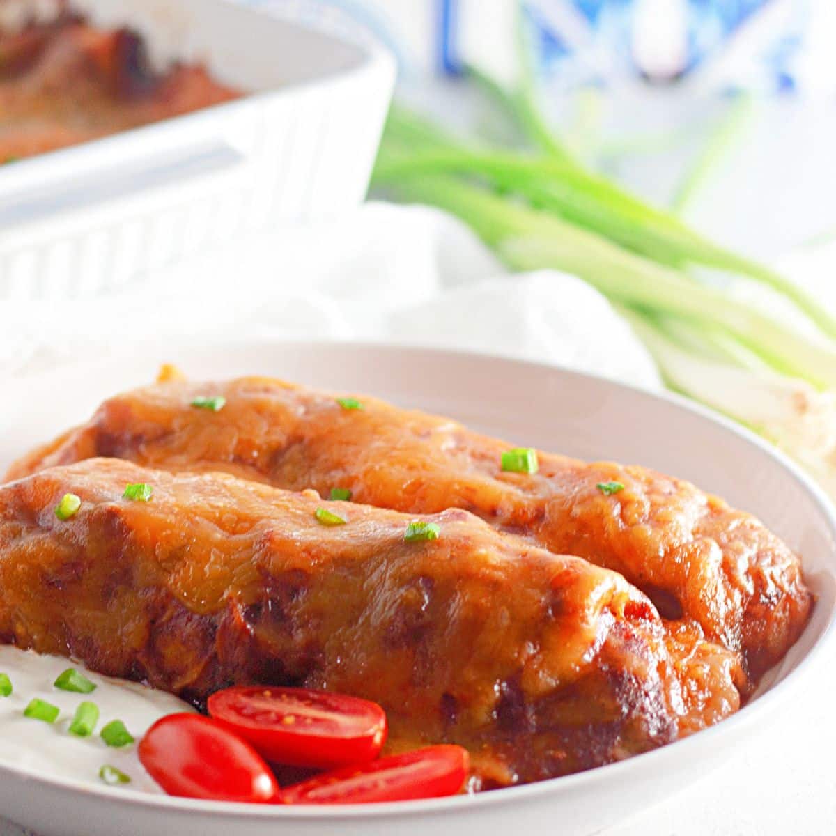 A plate of enchiladas with sour cream and tomatoes.