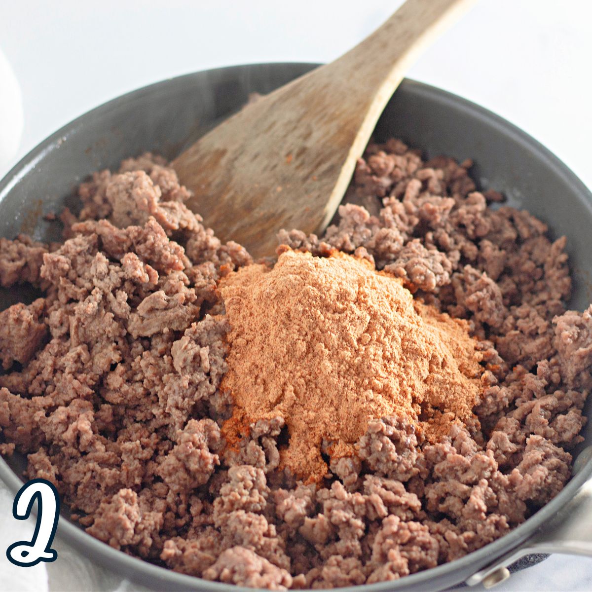 Ground beef and taco seasoning in a pan with a wooden spoon.