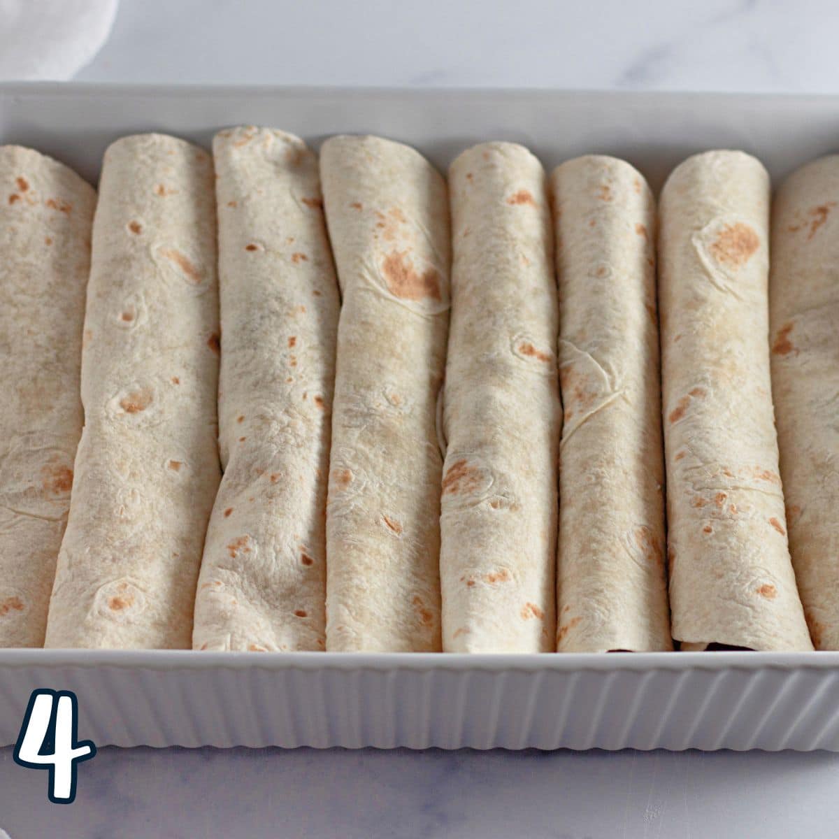 Flour tortillas filled with ground beef in a white baking dish.