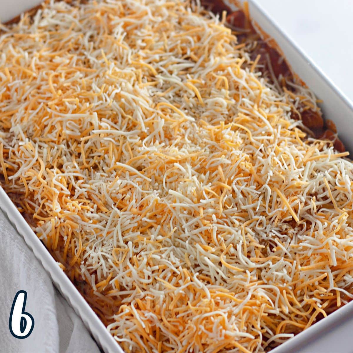 A white baking dish with shredded cheese on top  of enchiladas..