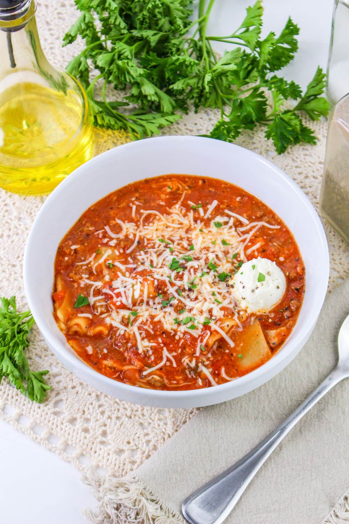 A bowl of lasagna soup with a spoon and basil.