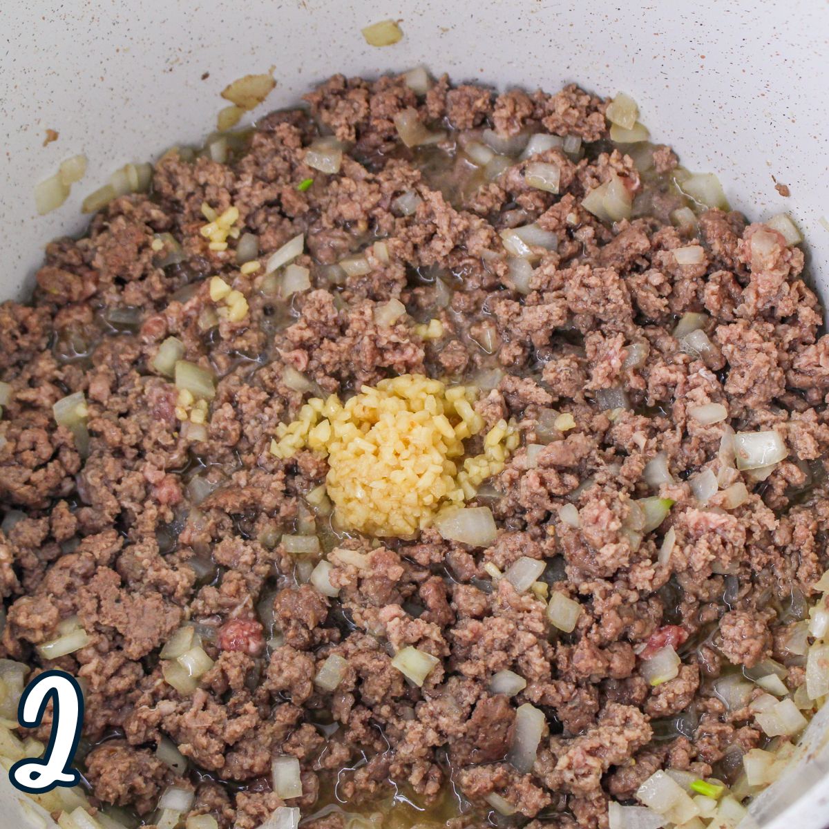 A bowl of browned ground beef and onions topped with garlic. 