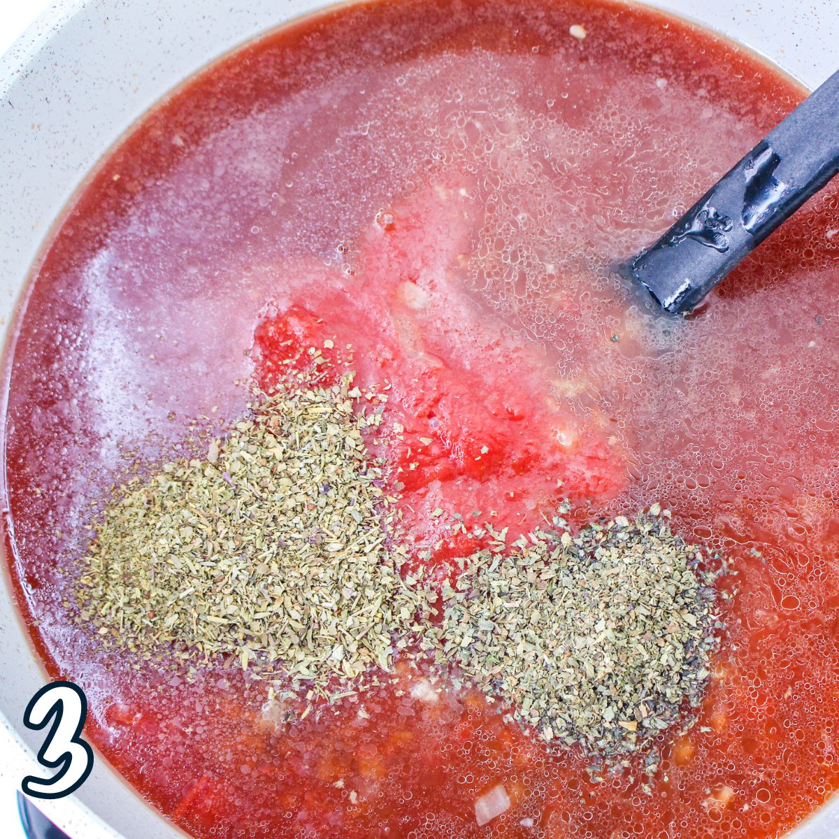 Spices added to a tomato based soup cooking in a Dutch oven. 