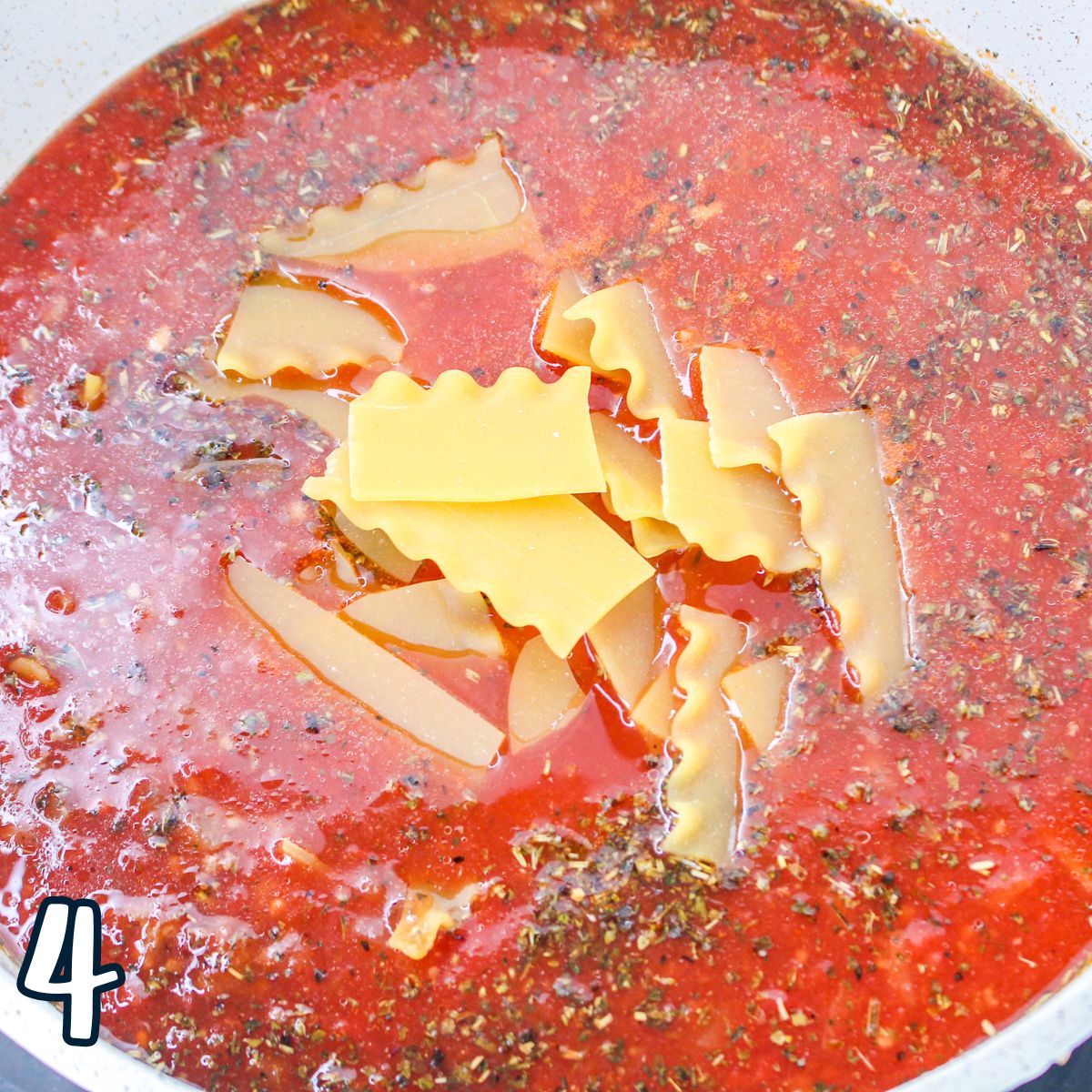 A pot of tomato sauce with broken lasagna noodles in it.