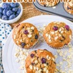 A plate and muffin tray with Banana Blueberry Oatmeal Muffins, alongside a bowl of fresh blueberries, rest gracefully on a patterned cloth.