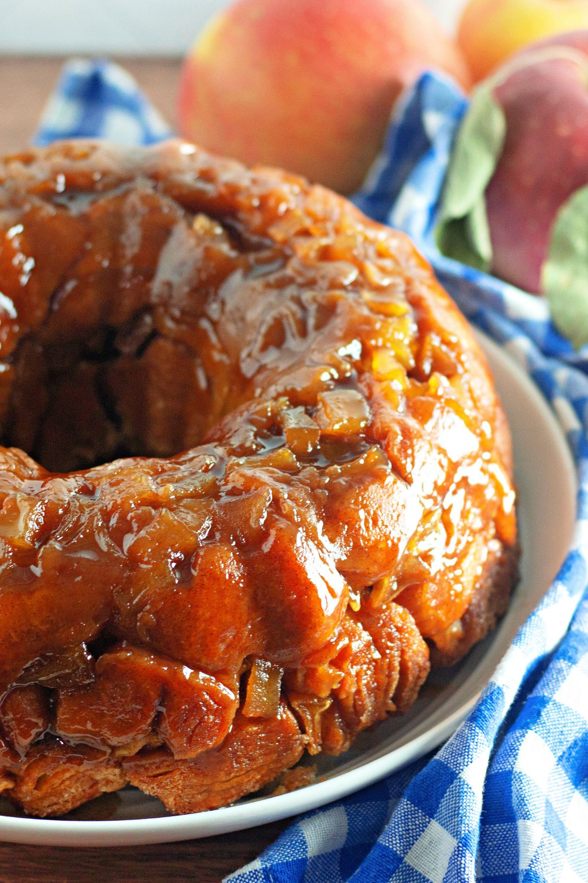 Glazed apple monkey bread on a plate with fresh apples in the background.