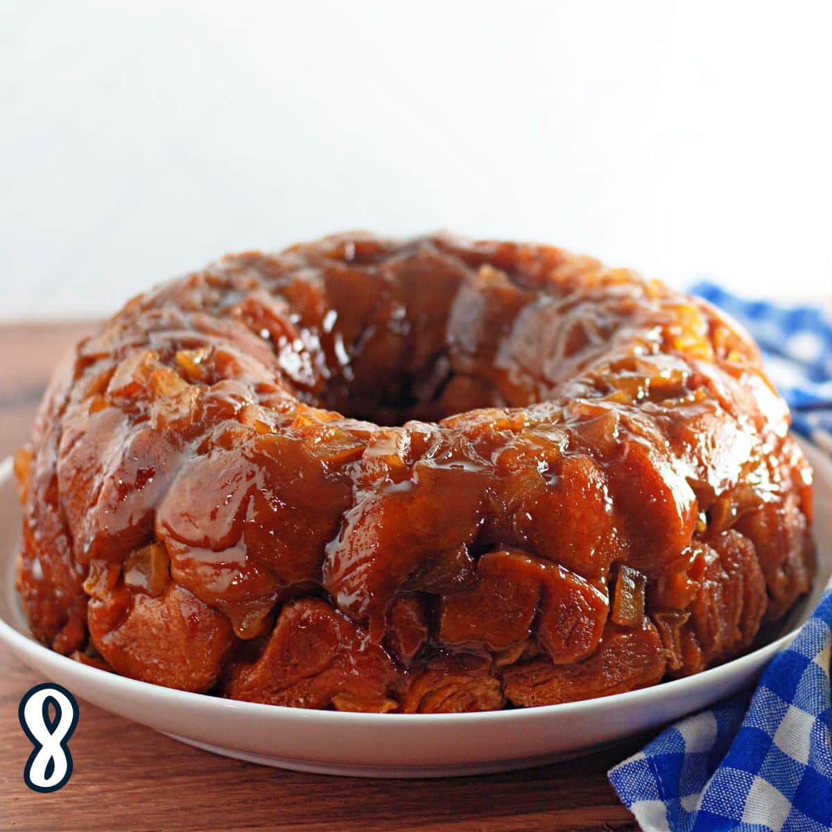 Glazed monkey bread on a white plate with a blue and white checkered napkin in the background.
