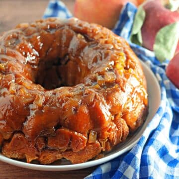 Caramel-glazed apple monkey bread on a blue and white checkered cloth with fresh apples in the background.
