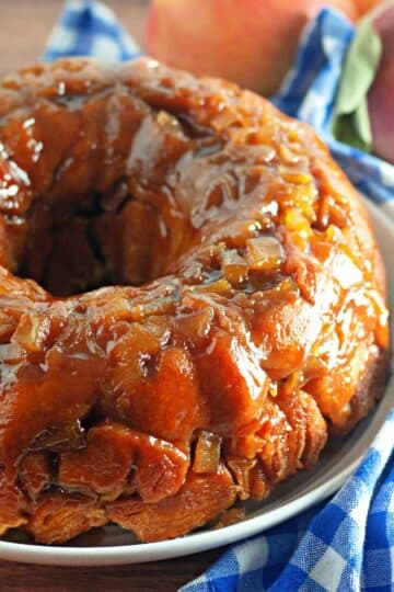 Caramel-glazed apple monkey bread on a blue and white checkered cloth with fresh apples in the background.
