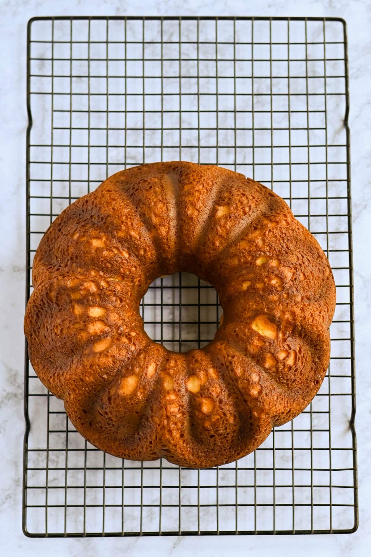 A bundt cake cooling on a wire rack on a marble countertop.