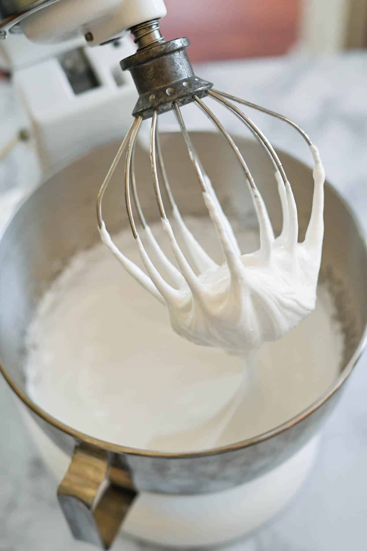 A stand mixer with a whisk attachment covered in marshmallow frosting. 