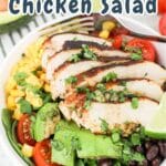 A colorful bowl of Southwest Chicken Salad with grilled chicken, black beans, corn, avocado, tomatoes, and lime wedges.