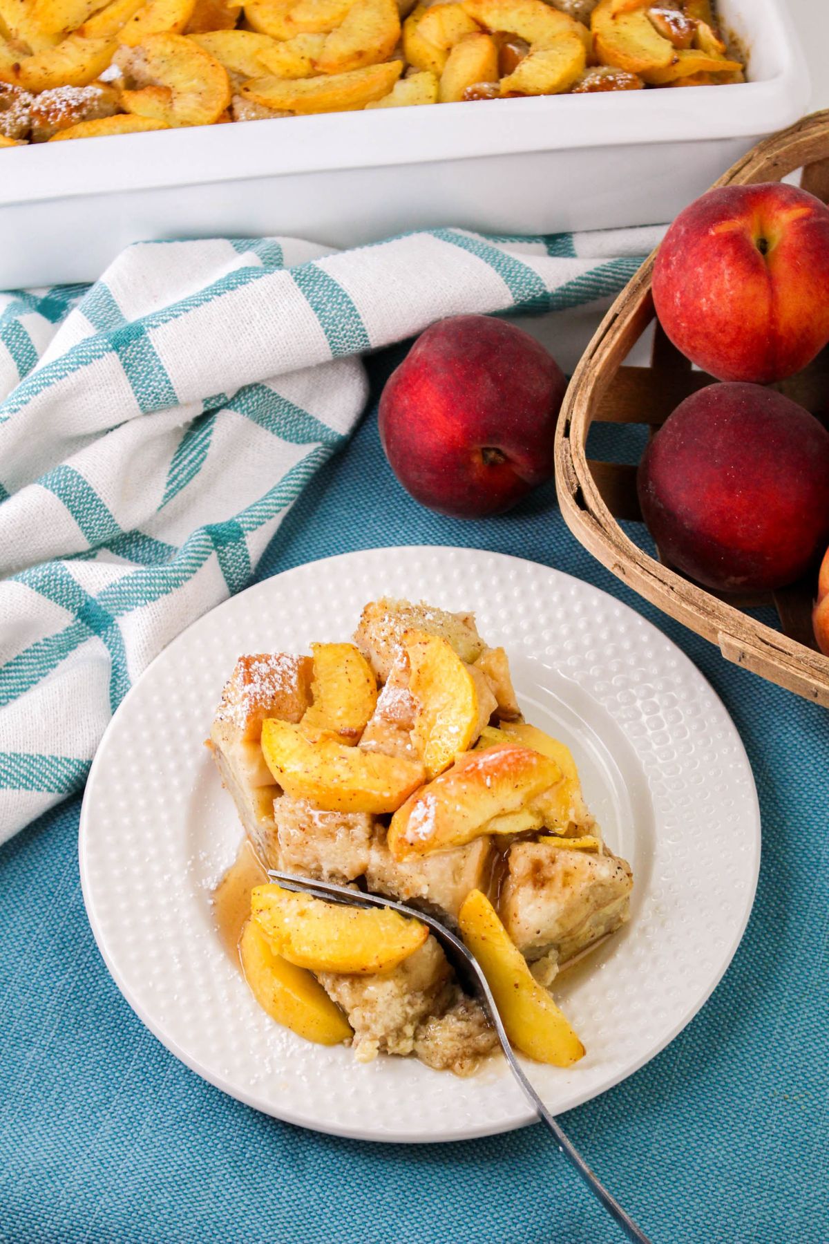 A plate of peach baked French Toast with a fork placed in it.. A white and teal towel is nearby on a blue surface.