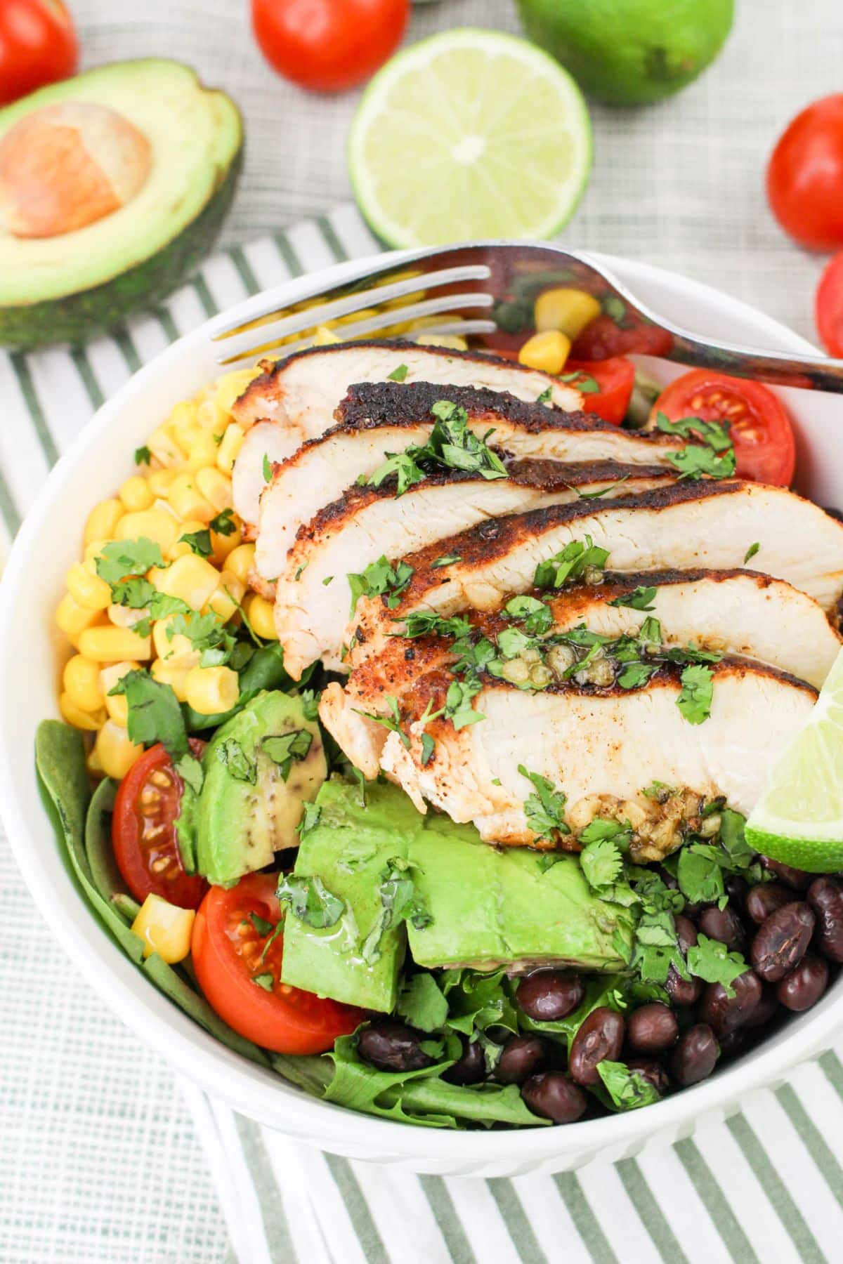 Bowl with grilled chicken, avocado, black beans, corn, tomatoes, and greens, garnished with lime and cilantro.