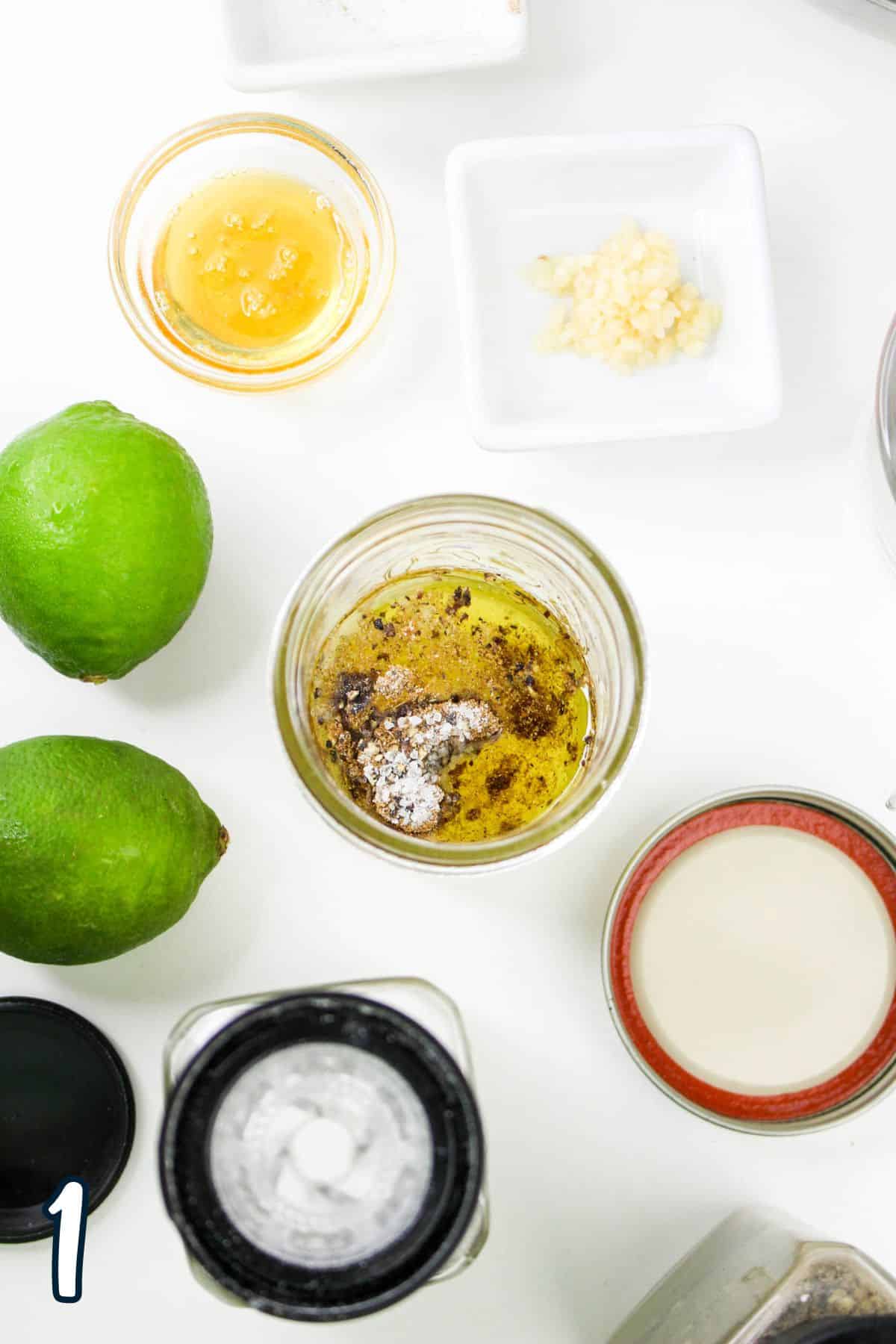 Ingredients including limes, honey, minced garlic, and various spices arranged around a glass jar on a white surface.