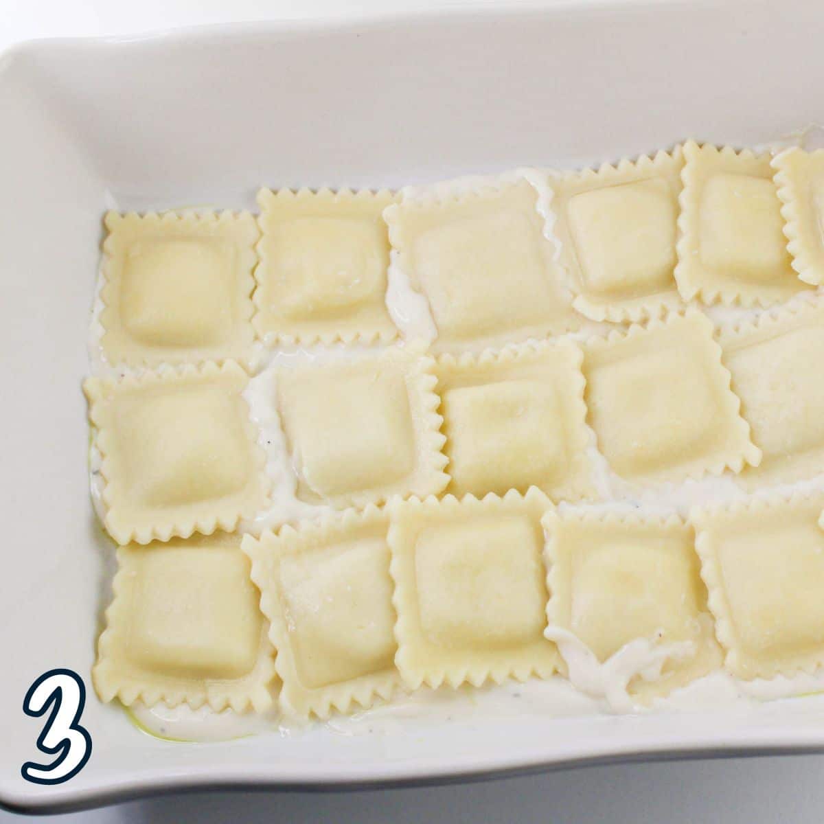 A baking dish filled with cooked ravioli arranged in a single layer on a light sauce. The number "3" is displayed in the bottom left corner.