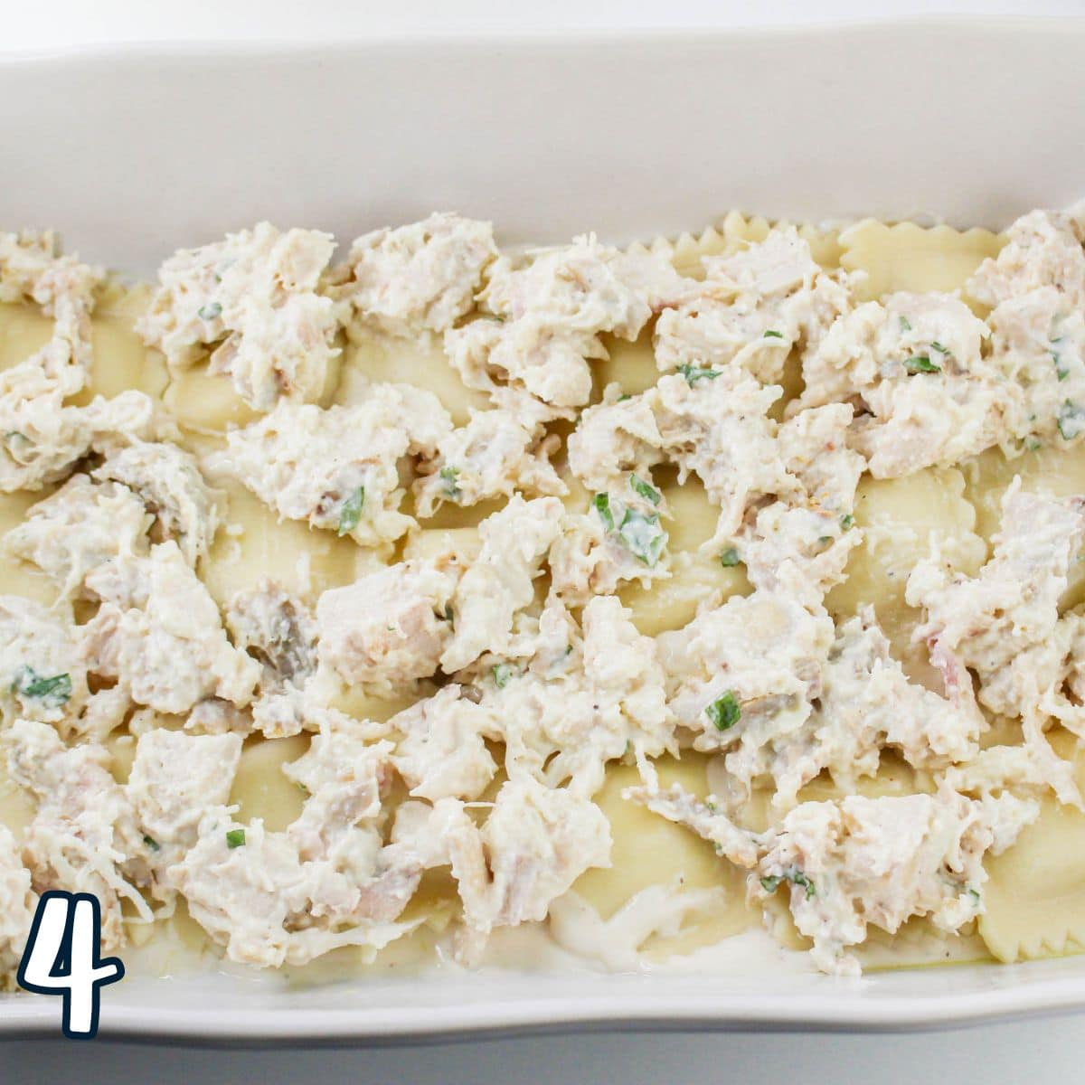 A white rectangular dish filled with layered pasta topped with a creamy chicken mixture. The number "4" is in the bottom left corner.
