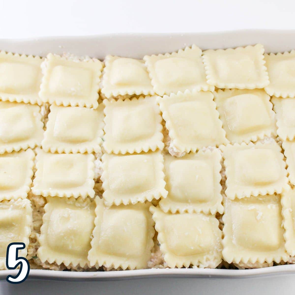 A baking dish filled with an even layer of cooked ravioli arranged in a grid pattern. The number 5 is displayed in the bottom left corner.