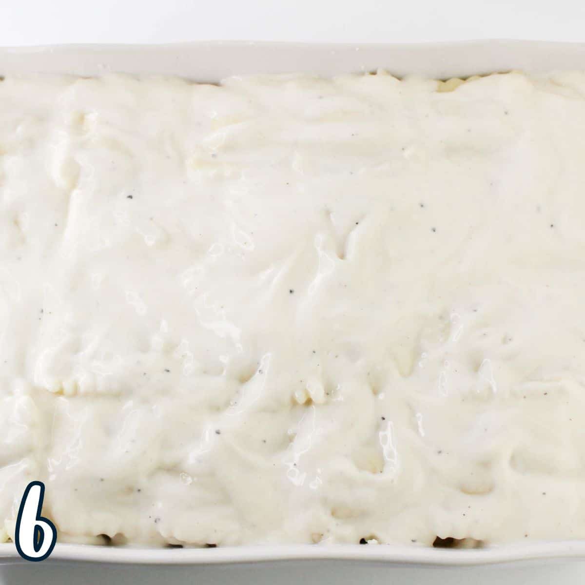 A baking dish filled with a layer of creamy white sauce over ravioli and chicken. A number "6" is in the bottom left corner.