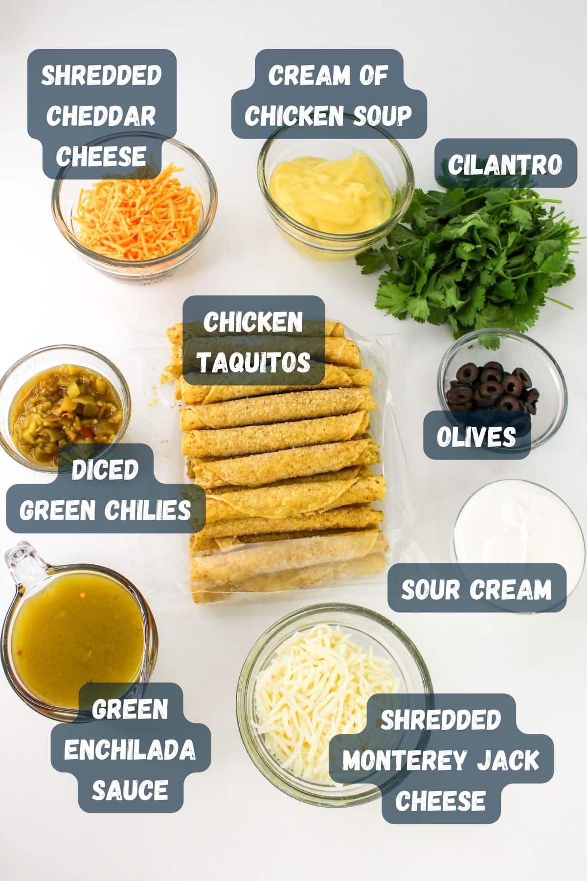 A layout of ingredients for a recipe including shredded cheddar cheese, cream of chicken soup, cilantro, chicken taquitos, olives, sour cream, shredded Monterey Jack cheese, green enchilada sauce, and diced green chilies.