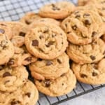 A pile of freshly baked chocolate chip cookies cooling on a wire rack.