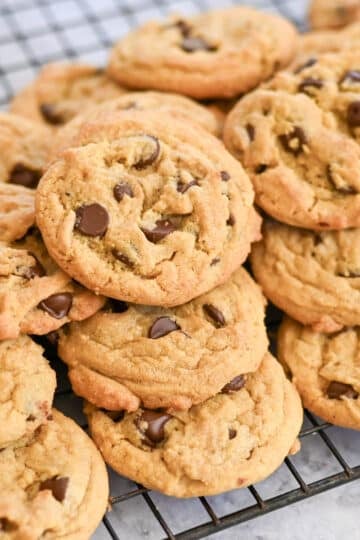 A pile of freshly baked chocolate chip cookies cooling on a wire rack.