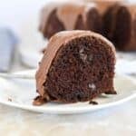 A slice of chocolate bundt cake with chocolate frosting on a white plate.