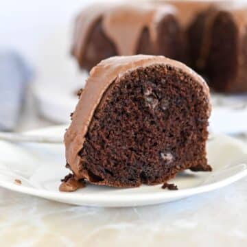 A slice of chocolate bundt cake with chocolate frosting on a white plate.