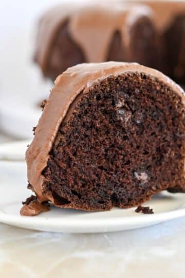 A slice of chocolate bundt cake with chocolate frosting on a white plate.