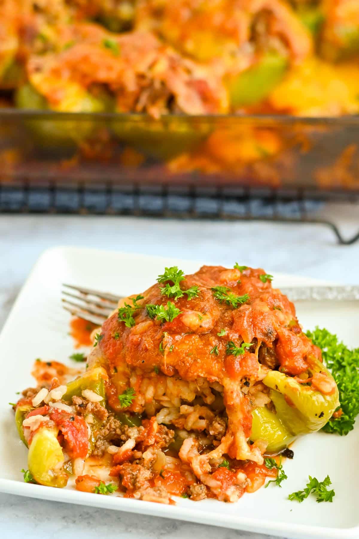 A plate with a stuffed green bell pepper topped with tomato sauce and parsley; a casserole dish in the background.
