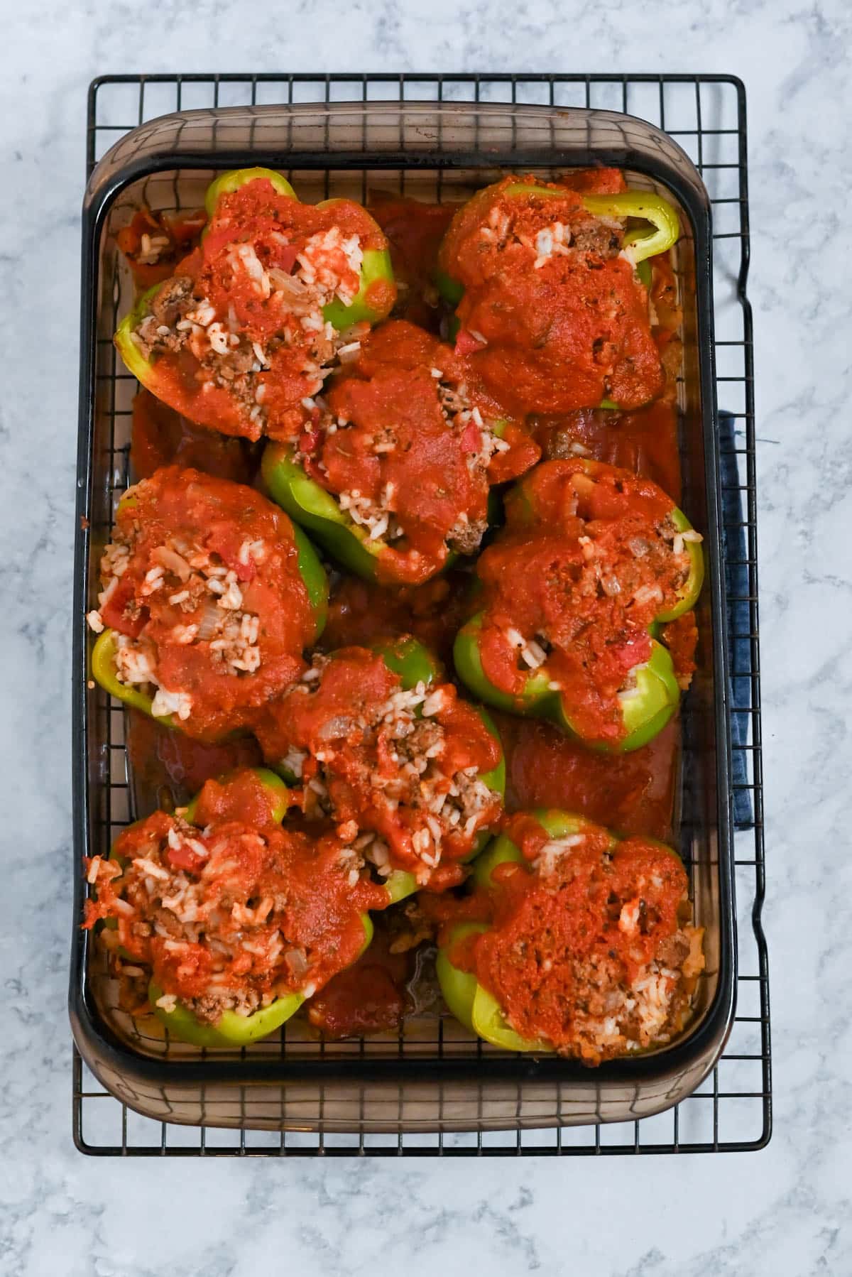 A baking dish with stuffed bell peppers topped with tomato sauce and rice, placed on a cooling rack.