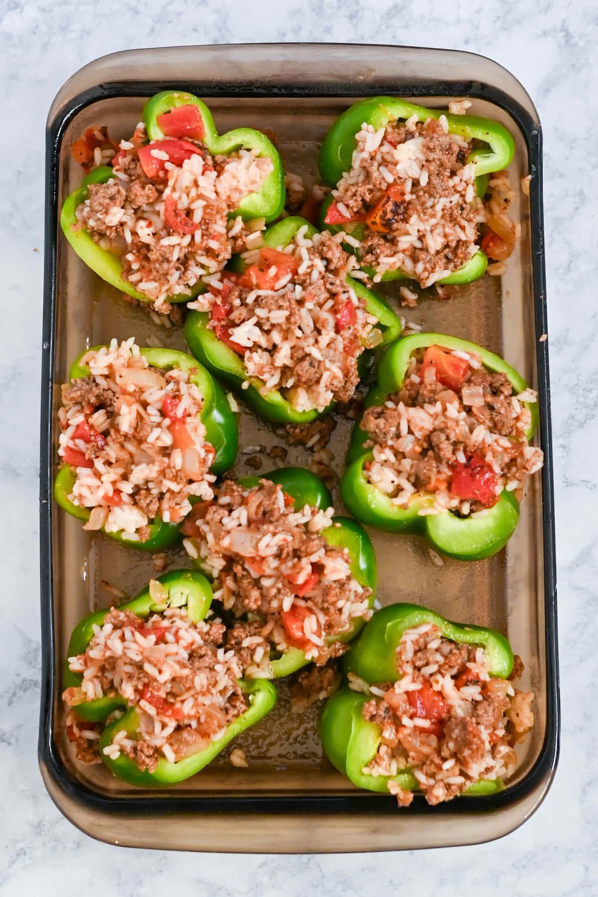 A dish of green bell peppers stuffed with rice, ground meat, and tomatoes, ready to be baked.