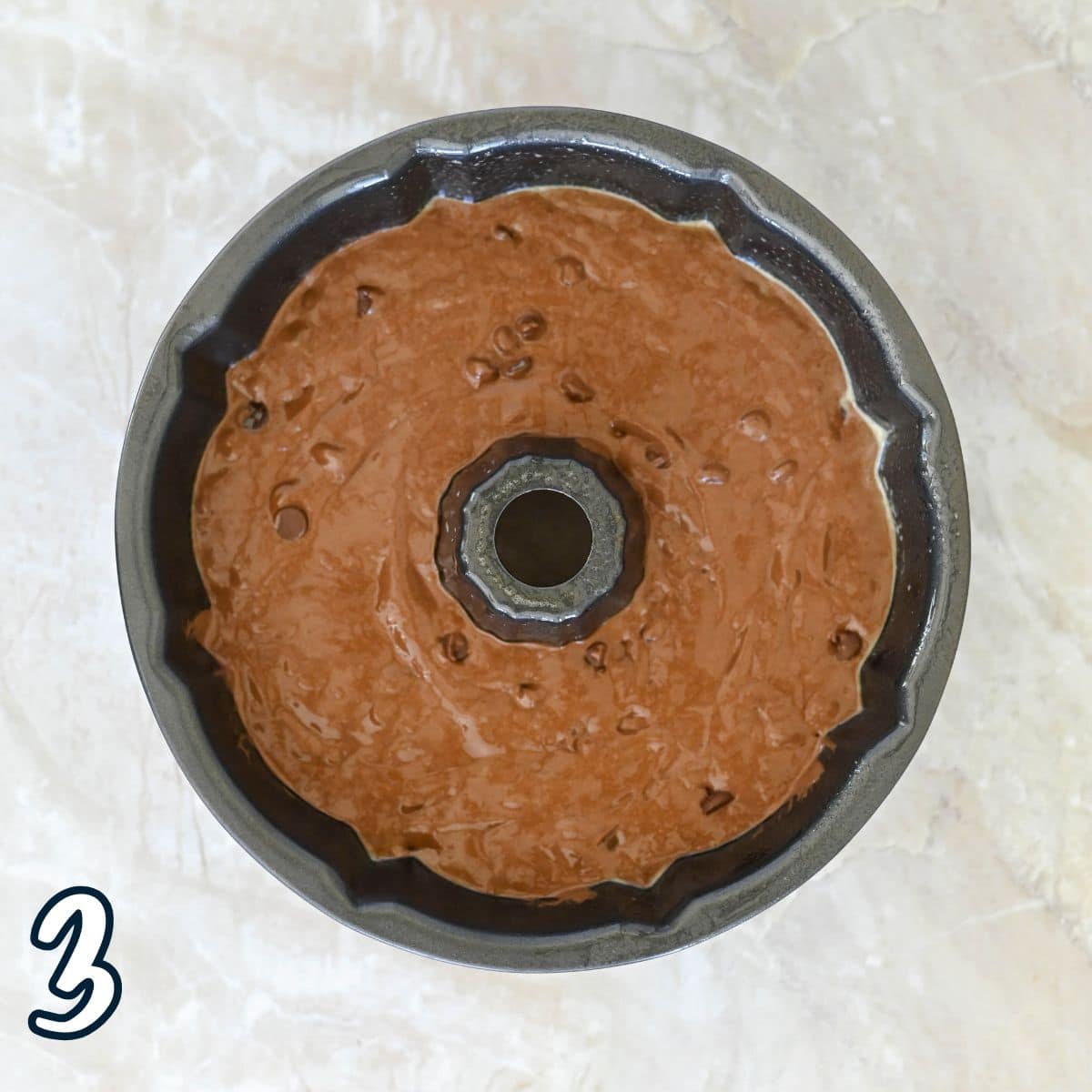 Chocolate batter in a Bundt pan, ready to bake, on a light marble surface. Number "3" in the corner.