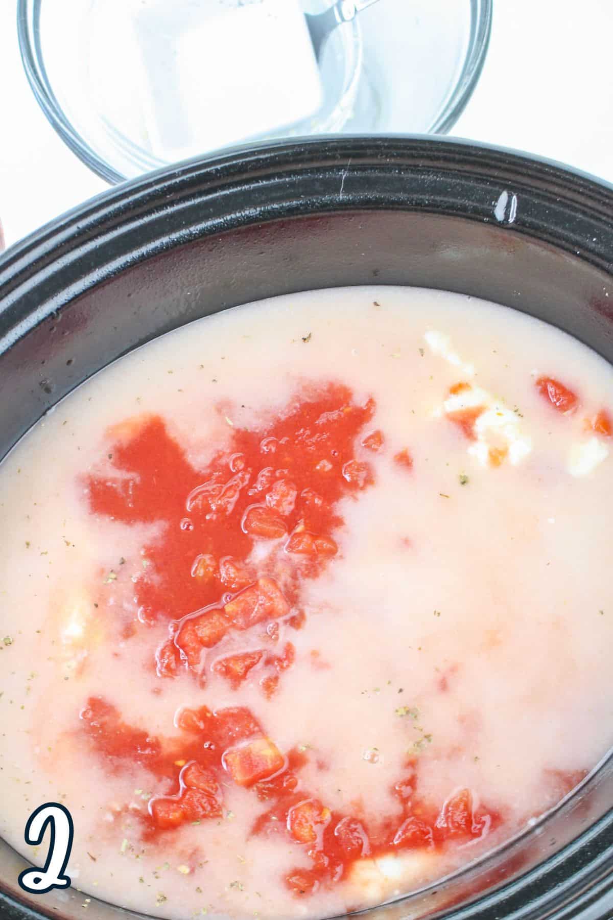 A slow cooker filled with diced tomatoes and white ingredients, with a glass bowl and a number 2 on the side.