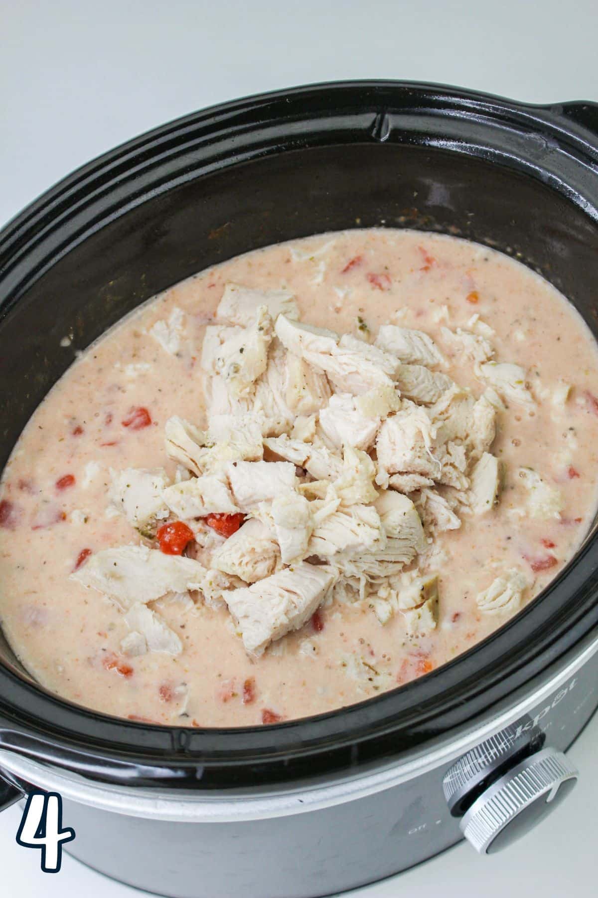 A slow cooker filled with a creamy chicken and tomato mixture, with shredded chicken on top. A number 4 is in the corner.