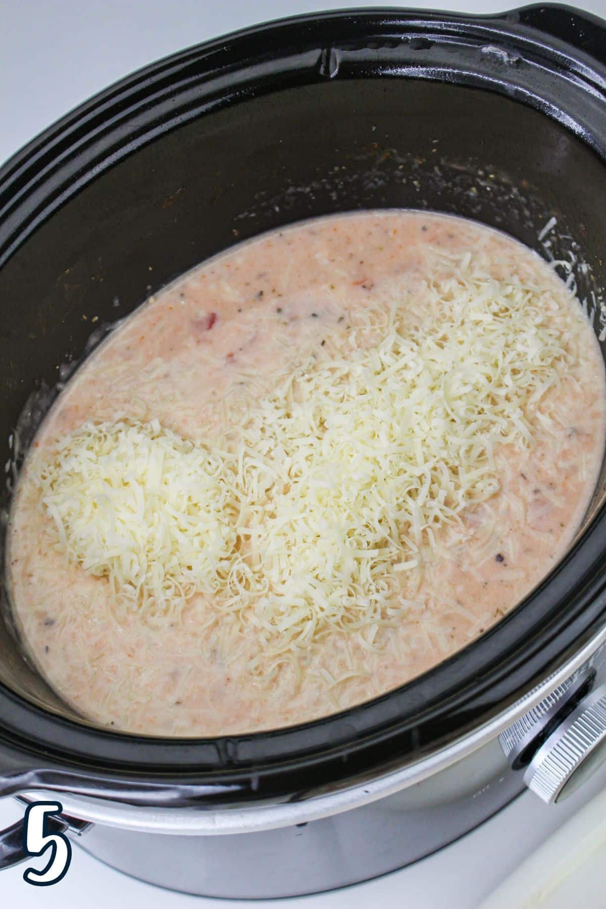 A slow cooker filled with creamy soup topped with shredded cheese, labeled with the number 5 in the bottom corner.