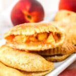 Close-up of peach hand pies with golden-brown crusts, showcasing warm, cinnamon-dusted fruit filling, on a white plate.