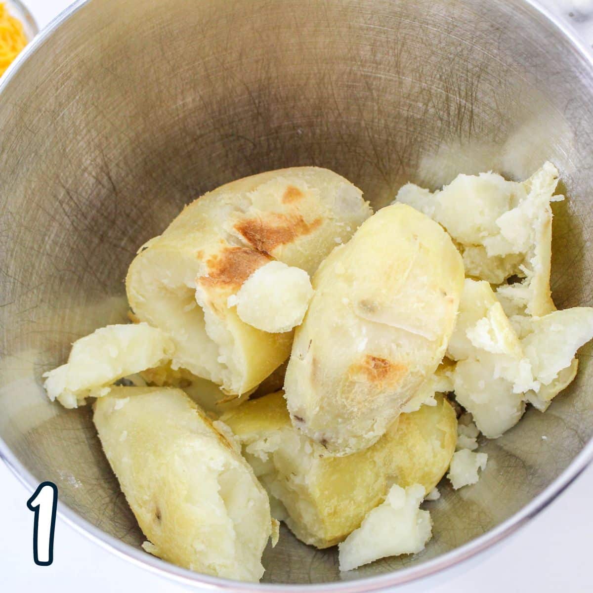 Baked potatoes in a mixing bowl, ready to be mashed; a small number "1" is at the bottom left.